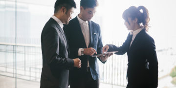 Three co-workers hold a business meeting in a bright office demonstrating the latest technological solutions.