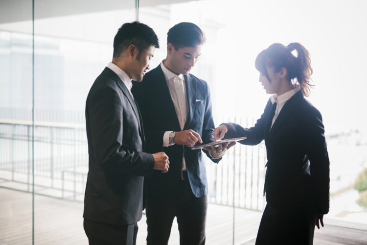 Three co-workers hold a business meeting in a bright office demonstrating the latest technological solutions.