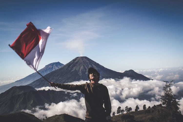Photo by Dio Hasbi Saniskoro: https://www.pexels.com/photo/man-wearing-black-crew-neck-sweater-holding-white-and-red-flag-standing-near-mountain-under-blue-and-white-sky-1009949/